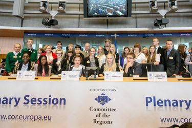 Brüsselisse preemiareisile tulnud kooliõpilased kolmapäeval Euroopa Liidu Regioonide Komitee istungitesaalis presiidiumi laua taga. Keskel Euoopa Liidu Regioonide Komitee presidendi koha peal istub Põlva ühisgümnaasiumi kümnenda klassi tüdruk Helen Rebane, tema kõrval klassikaaslane Kirke Prii. Komitee president ise seisab Kirke selja taga. Tagaplaanil on tüdrukute juhendaja, inglise keele õpetaja Tiit Rästa, tema ees seisavad Kiviõli keskkooli õpilased Kristin Kont ja Liisa Vilumets. 	  Foto: Euroopa Liidu Regioonide Komitee
